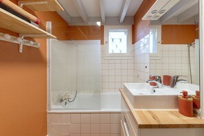 A bathroom with a glass-enclosed shower, a white sink with a mirror, and a wooden shelf above the sink.