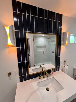 A bathroom with a large mirror, a white sink, and two wall-mounted lights. -  Bakersfield Luxe Stay • Stylish & Serene (Bakersfield)