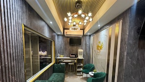 Una habitación de hotel moderna con un espejo grande, un sofá verde, una pequeña zona de bar y una lámpara decorativa en el techo.