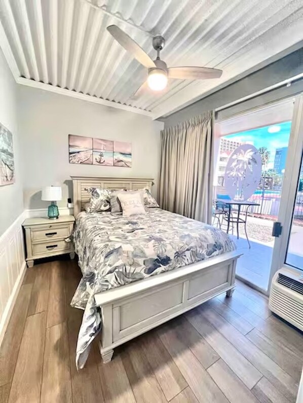 A bedroom with a bed, a nightstand, a ceiling fan, and a view through a glass door to the outside.