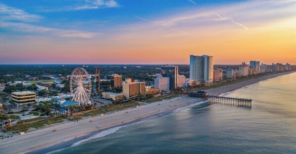 A coastal cityscape with a prominent Ferris wheel, high-rise buildings, and a beach. - Beach Haven, Only 5-Star Reviews, 1st Floor Condo! (Myrtle Beach)