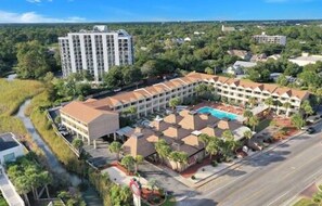 A hotel with a central courtyard, a swimming pool, and a tall building in the background. - Beach Haven, Only 5-Star Reviews, 1st Floor Condo! (Myrtle Beach)