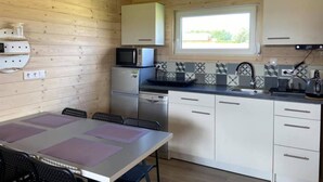 A compact kitchen with a microwave, refrigerator, and dishwasher. There is a window providing natural light, and the room has wooden walls and a tiled backsplash. - Holiday Home in Mielenko Near Seaside Beach (Mielno)