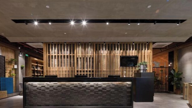 Ein Empfangsbereich modernen Designs mit einer Wand aus Holzleisten, einer Rezeption mit Steinoptik und einem an der Wand montierten Flachbildfernseher.