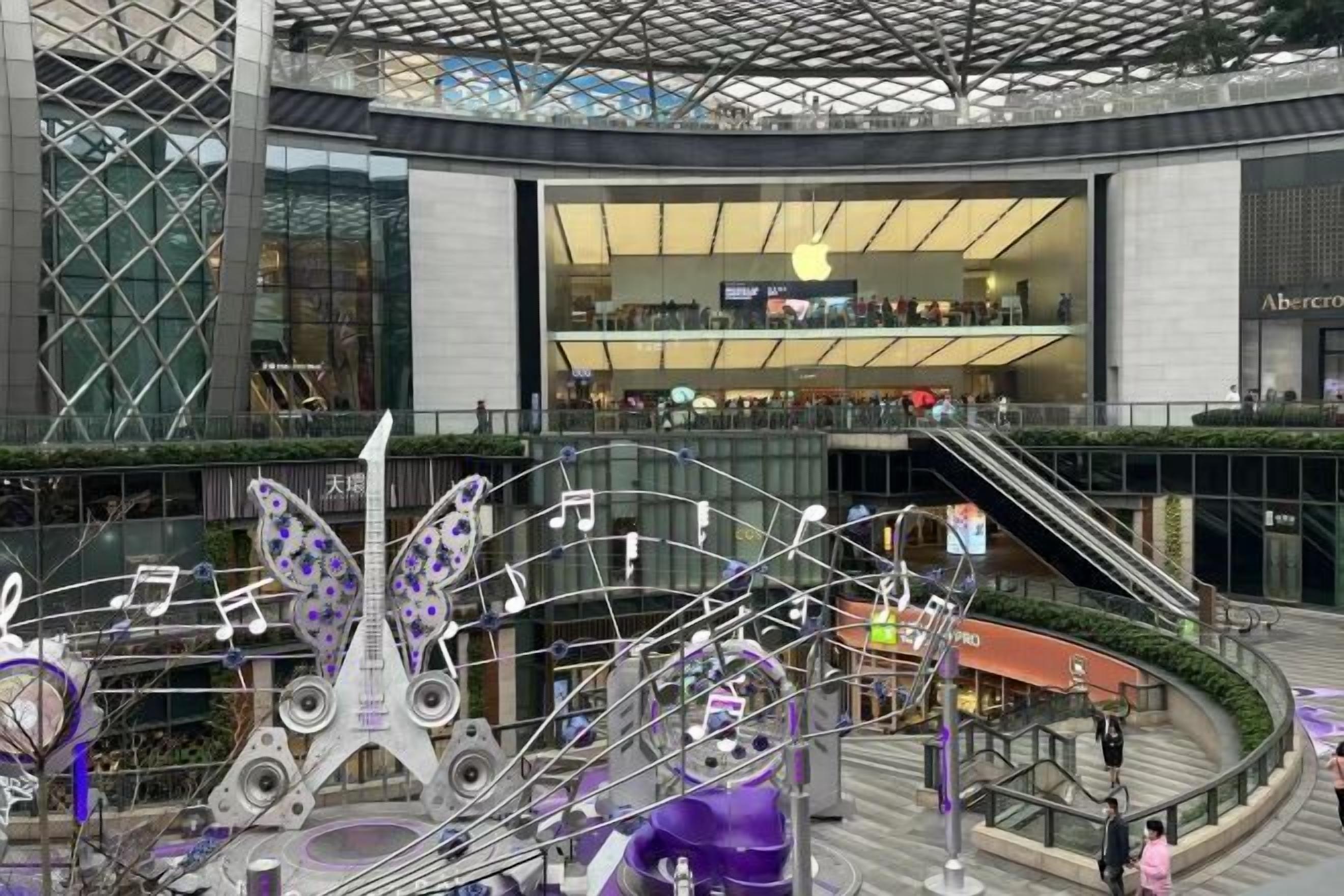 Ein modernes Einkaufszentrum mit einem zentralen Atrium, Fahrtreppen und einer dekorativen Metallskulptur.