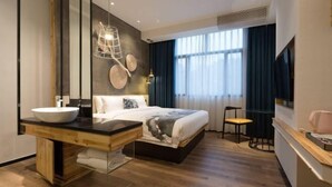 Ein modernes Hotelzimmer mit einem großen Bett, einem Holznächtigungsschrank mit Waschbecken und einem großen Spiegel sowie einem Fernseher an der Wand.