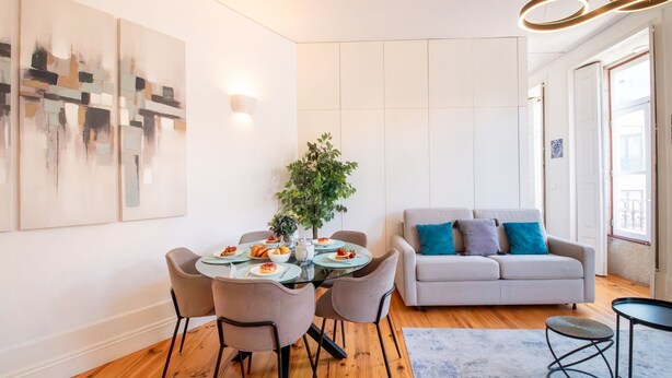 A modern living room with a dining area, featuring a grey sofa, a small round table, and a dining table with chairs. - Bright Flat few steps to Aliados Av by LovelyStay (Porto)