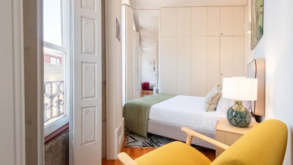 Hotellihuone, jossa on sänky, yöpöytä, tuoli ja ikkuna, josta on näkymä parvekkeelle.