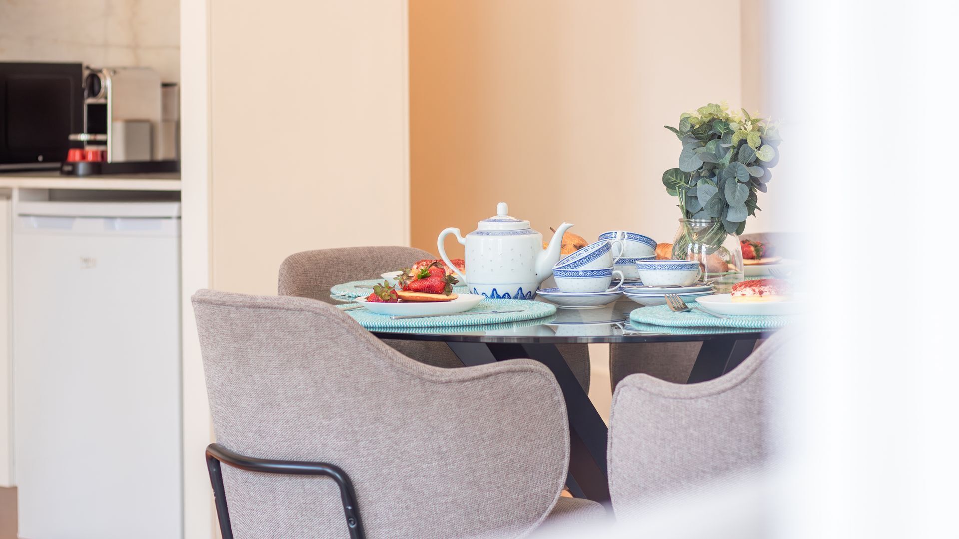 A dining table set with plates, a teapot, and a vase with flowers.