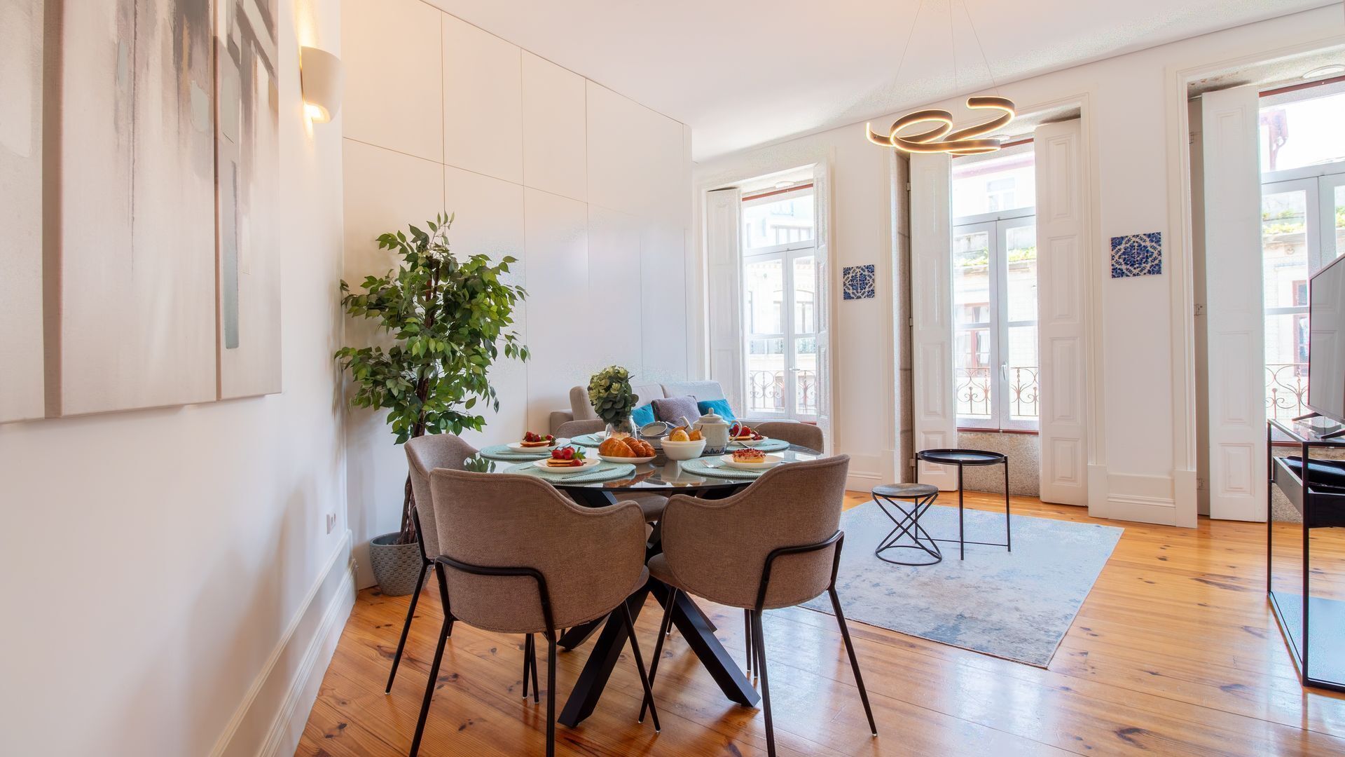 Een eethoek met een tafel voor vier personen, omringd door stoelen, een potplant en uitzicht op buiten.