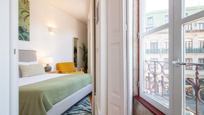 A hotel room with a bed, a chair, a lamp, and a view of the street through a window. - Bright Flat few steps to Aliados Av by LovelyStay (Porto)