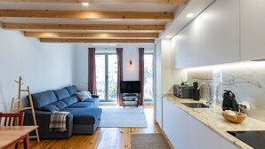 Una cocina moderna con encimera de mármol, horno empotrado y fregadero. Hay una mesa de comedor de madera con sillas, un sofá azul y un televisor en la sala de estar.