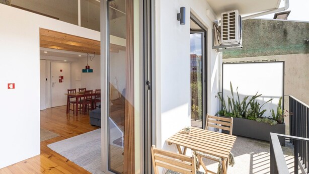Un interior moderno con piso de madera, una zona de comedor con sillas y una escalera que conduce a un nivel superior.