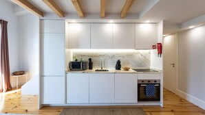 Cocina compacta con armarios blancos, salpicadero de mármol, horno empotrado y techo de madera.