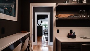 A modern kitchen with wooden countertops, a dining area with chairs, and a view into the dining room through a doorway.
