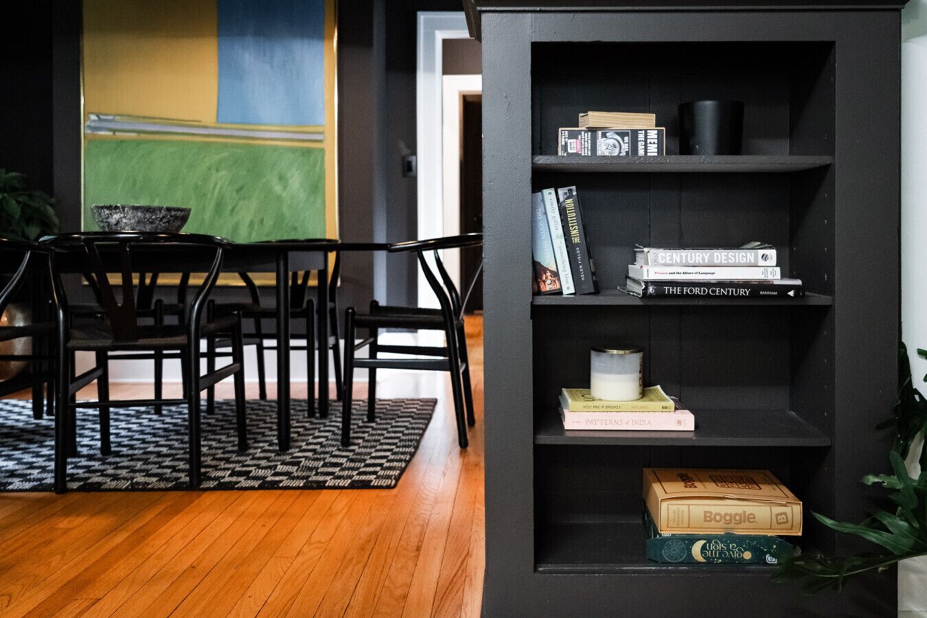 Un intérieur moderne avec une bibliothèque noire, une table à manger avec des chaises et un tapis à motifs.