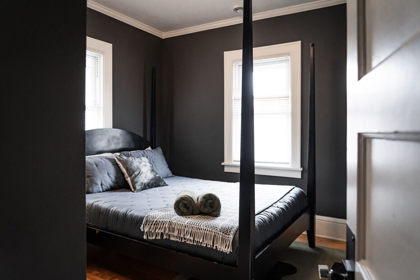 Une chambre à coucher avec un lit à baldaquin, des murs de couleur sombre et deux fenêtres équipées de stores.