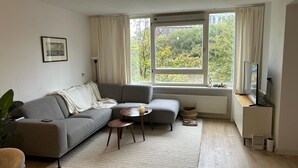 Een moderne woonkamer met een grijze bank, een klein rond tafeltje en een tv op een meubel.