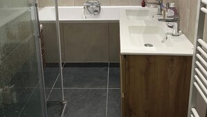 Een moderne badkamer met een douchecabine van glas, een vrijstaand bad en een houten wastafelmeubel met een wastafel.