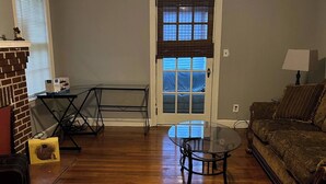 A living room with hardwood flooring, a glass coffee table, a sofa, a fireplace, and a door with a window. - Big House on Broadway (Jacksonville)