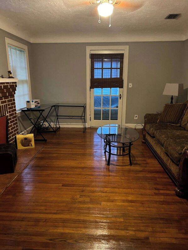A living room with hardwood flooring, a glass coffee table, a sofa, a fireplace, and a door with a window.