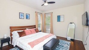 Een slaapkamer met een bed, een plafondventilator, een spiegel en een televisietoestel.