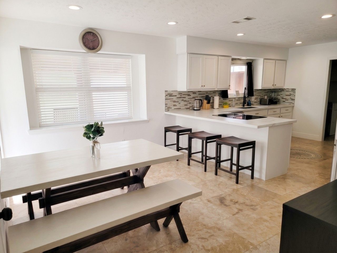 A modern kitchen with white cabinetry, a central island with stools, and a dining area with benches.