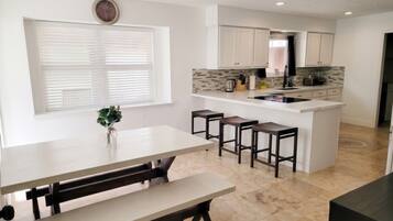 A modern kitchen with white cabinetry, a central island with stools, and a dining area with benches.