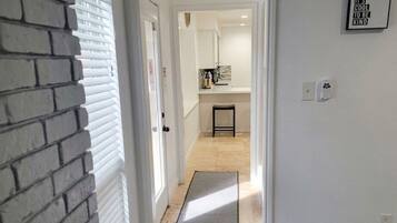 A hallway leading to a kitchen with a door, a rug, and a framed quote on the wall.