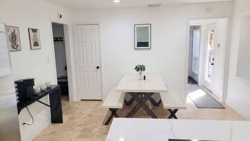 A modern kitchen with a white countertop, a black shelf, and a white dining table with benches.