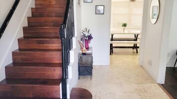 A staircase with a wooden finish and black handrails, leading to a room with a tiled floor and a bench.