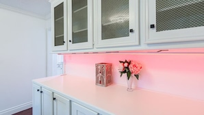 Una cocina con armarios blancos, encimera rosa y un florero con flores.