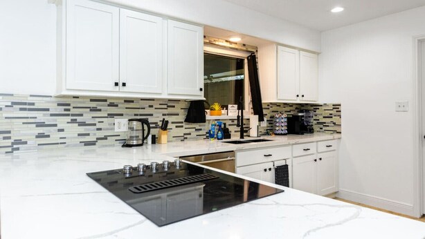 A modern kitchen with white cabinets, a black stove, and a tiled backsplash. - Pool | BBQ | Game Room | Gym | Patio | Workspace (Houston)