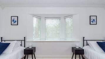 A bedroom with two beds, a window with blinds, and two bedside tables.