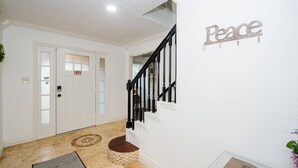 A clean, white interior with a staircase, a 'Peace' sign on the wall, and a doormat. - Pool | BBQ | Game Room | Gym | Patio | Workspace (Houston)