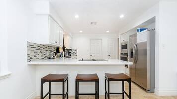 A modern kitchen with white cabinets, a tiled backsplash, a stainless steel refrigerator, and three wooden bar stools.