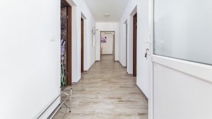 A narrow hallway with white walls and a wooden floor, leading to a door at the end.