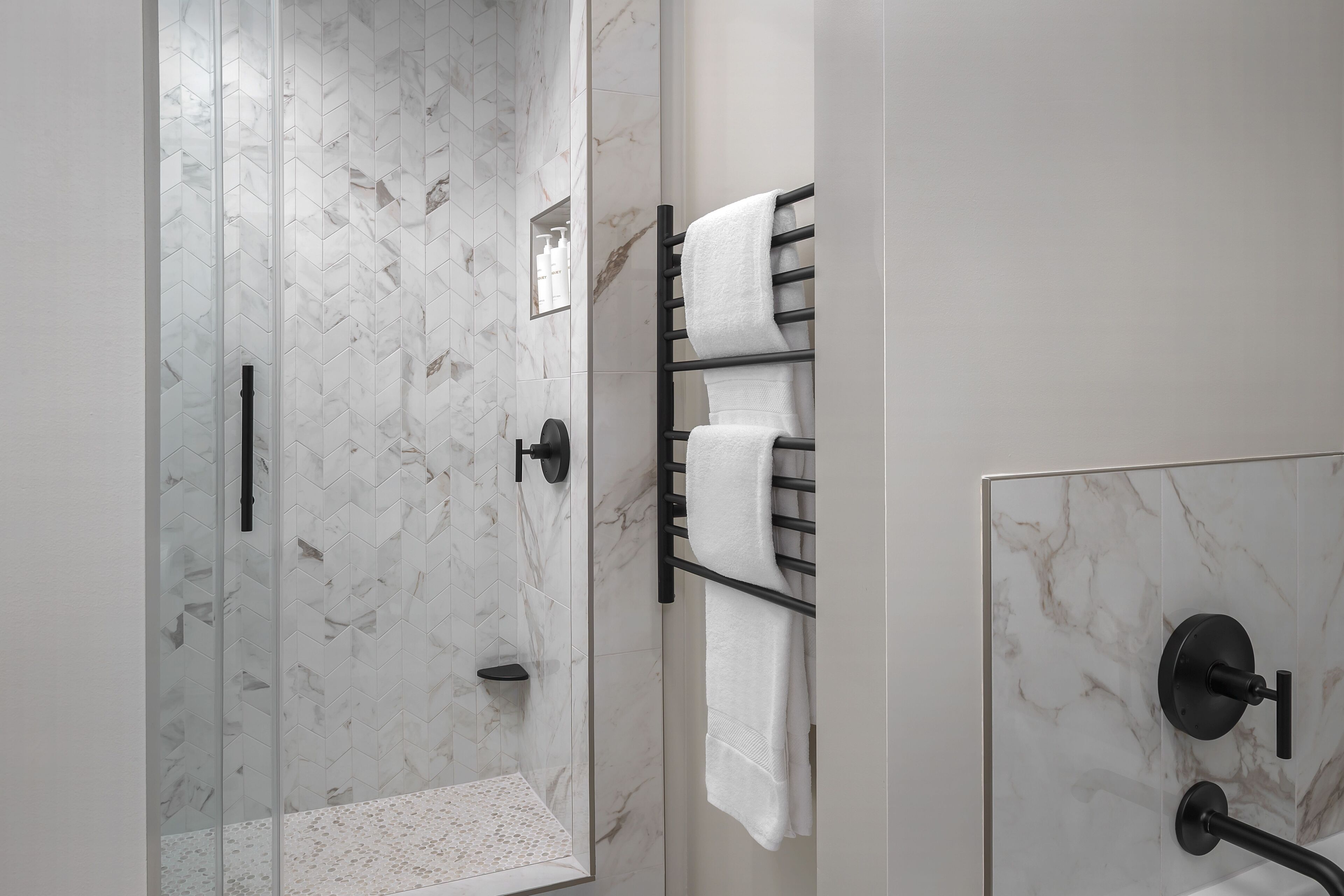 Un baño moderno con cabina de ducha de vidrio, paredes de mármol y un perchero con varias toallas.