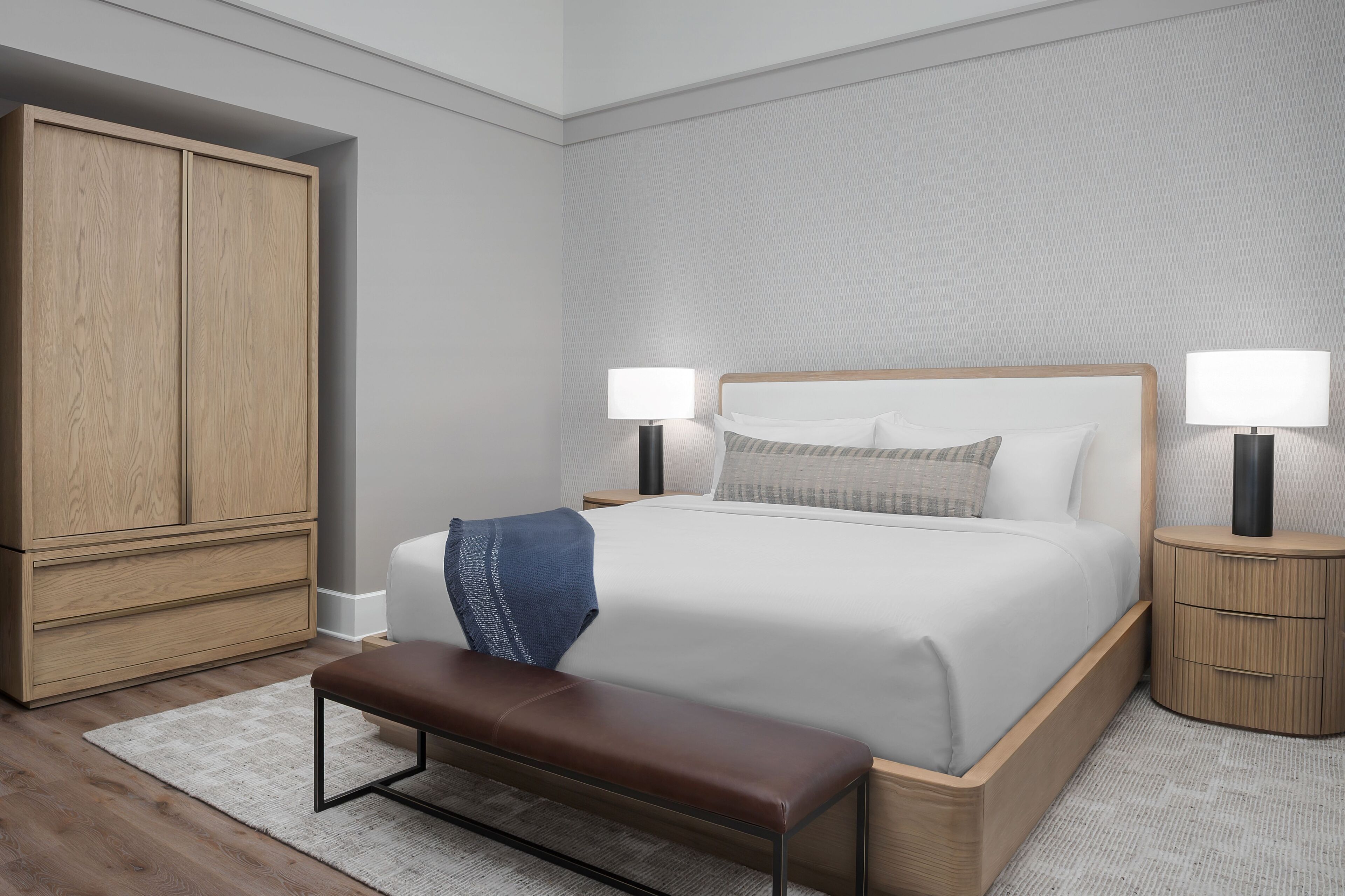 Ein modernes Schlafzimmer mit einem großen Bett, Nachttischen, einer Bank und einem Kleiderschrank.