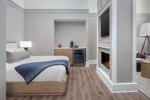 A modern hotel room with a bed, a TV mounted on the wall, a fireplace, and a small kitchenette area. - The Inn at Dayton (Dayton)