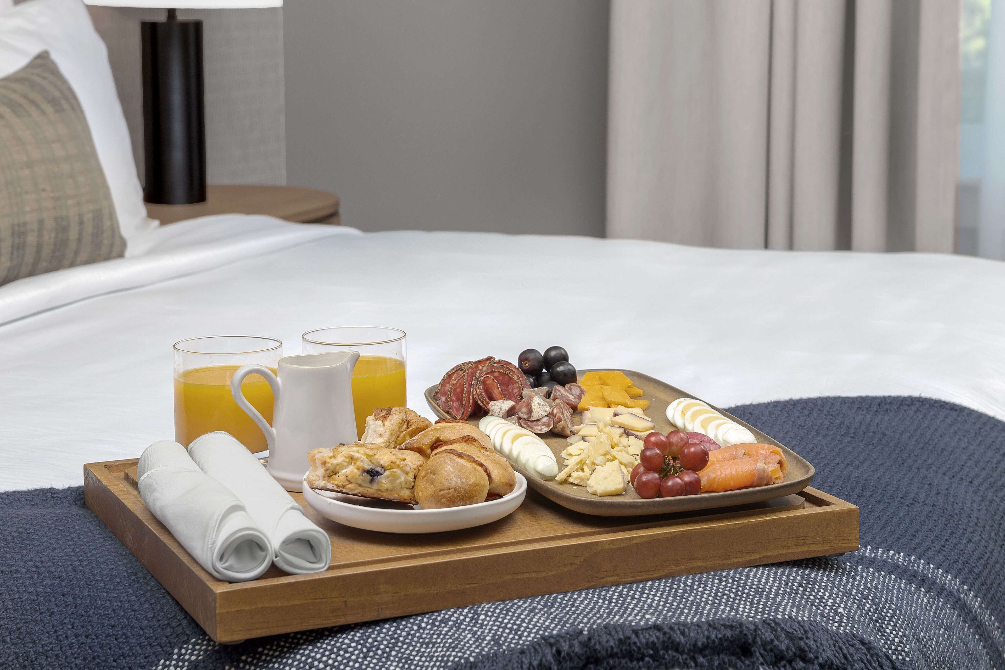 A breakfast tray with eggs, sausages, cheese, and fruit on a bed.