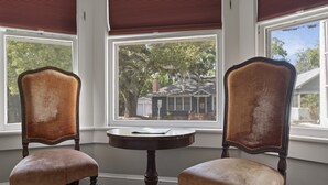 Zwei gepolsterte Stühle mit Holzgestell und ein kleiner runder Tisch dazwischen, vor einem Fenster mit Blick auf ein Haus und Bäume.