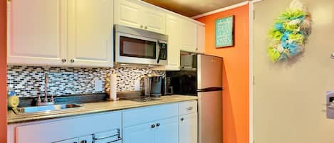 A kitchen with white cabinets, a microwave, a refrigerator, and a backsplash with black and white tiles.