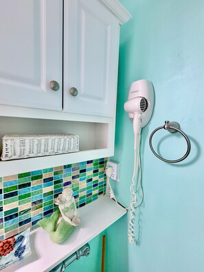 A bathroom with a white cabinet, a white hairdryer, a towel ring, a mosaic tile backsplash, and a decorative ceramic piece.