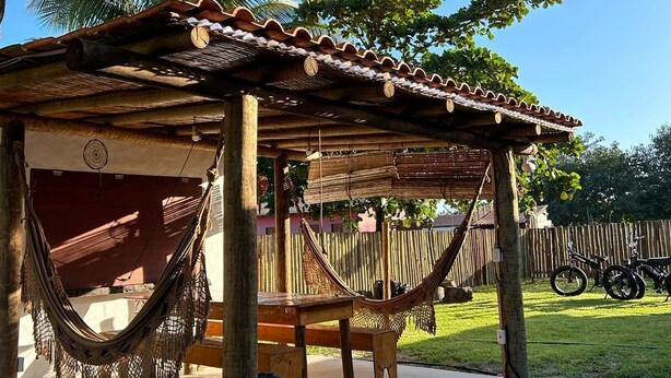A wooden structure with a tiled roof, a hammock, and a bicycle in the background. - Vila Santa Fé Caraíva  (Porto Seguro)