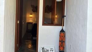 A hallway with a wooden door, a hanging woven light fixture, a wall-mounted mirror, and a decorative wall piece. - Vila Santa Fé Caraíva  (Porto Seguro)