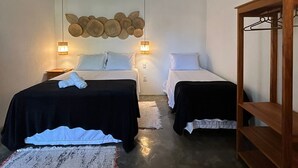 A room with two beds, a hanging light fixture, a wall-mounted air conditioner, and a wooden shelf. - Vila Santa Fé Caraíva  (Porto Seguro)