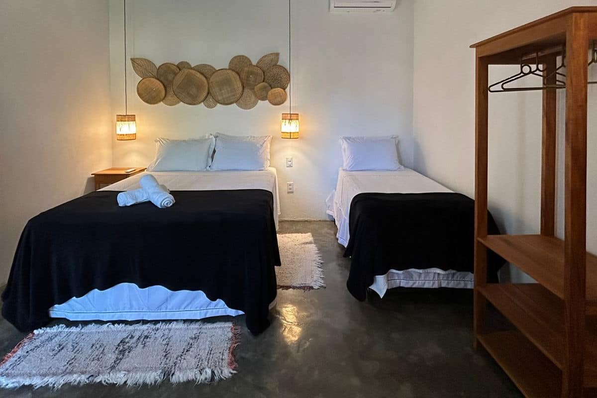 Une chambre avec deux lits, un luminaire suspendu, un climatiseur fixé au mur et une étagère en bois.