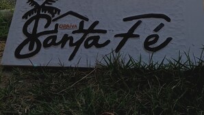 A sign with the text "SANTA FE" in a stylized font, placed on grass in an outdoor setting. - Vila Santa Fé Caraíva  (Porto Seguro)