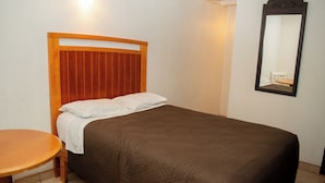 Un lit simple avec une tête de lit en bois, une table ronde en bois et un miroir accroché au mur.